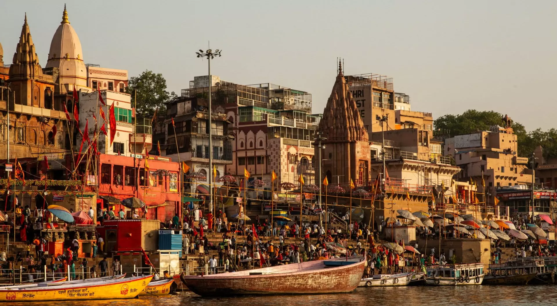 View of the Ganges River with the ghats leading down and boats on the river, as well as pilgrims crowding its edges in Varanasi, India.