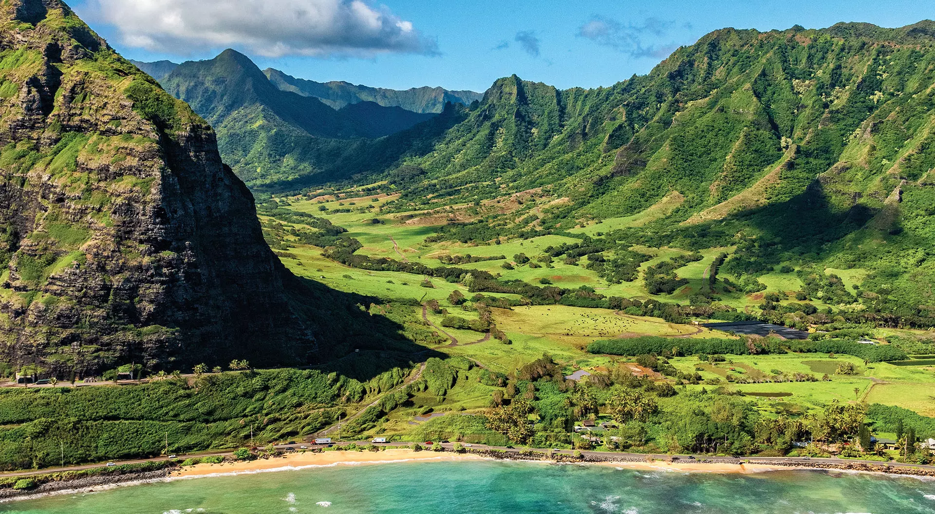 Kualoa Ranch, O'ahu, Hawai'i green mountains leading to sandy beach and blue waters in Hawaii