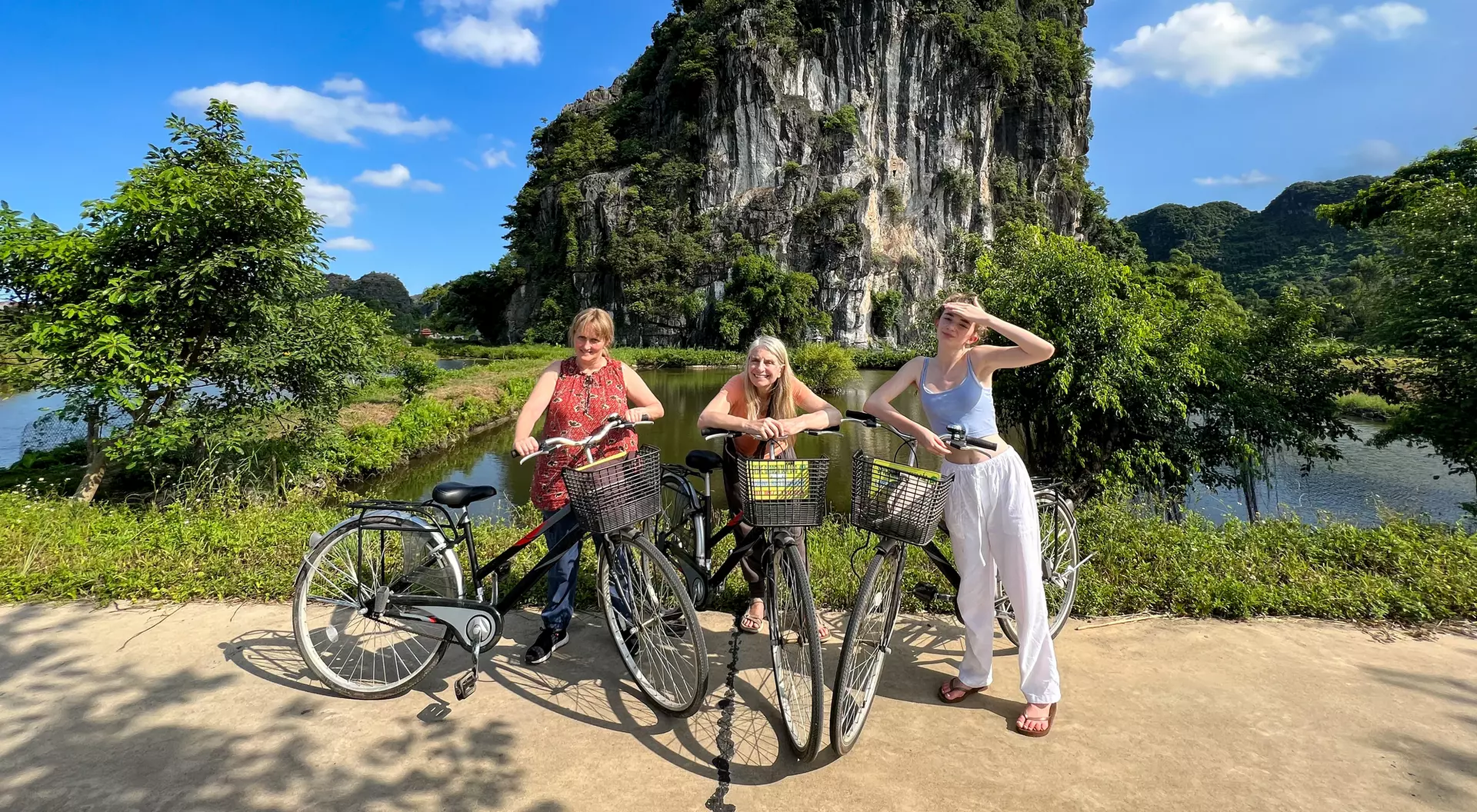 A group of women pose with their bikes in front of limestone hills in Ninh Binh, Vietnam.