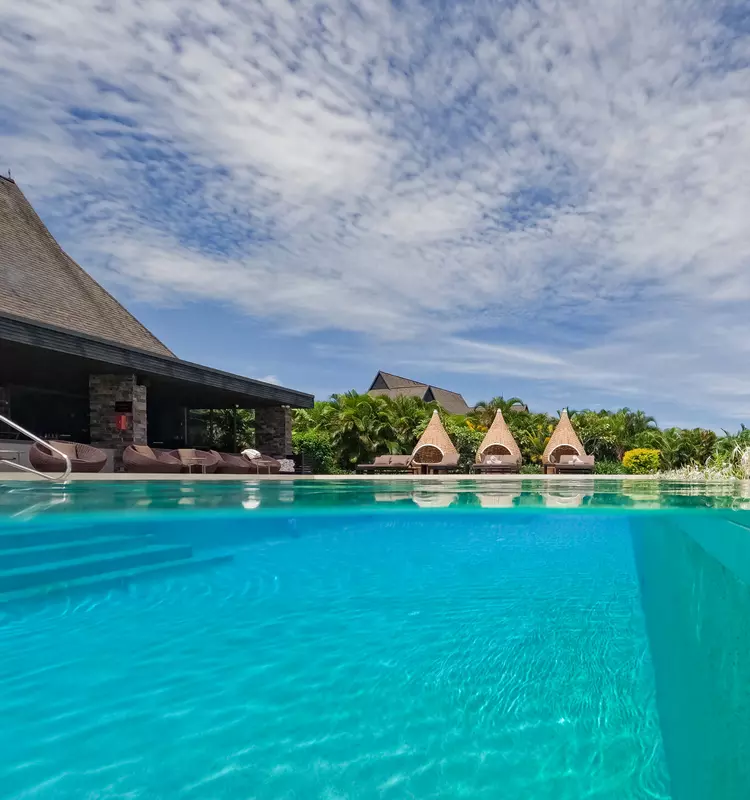 A beautiful pool-side cabana under a sunny sky, surrounded by lush palms.