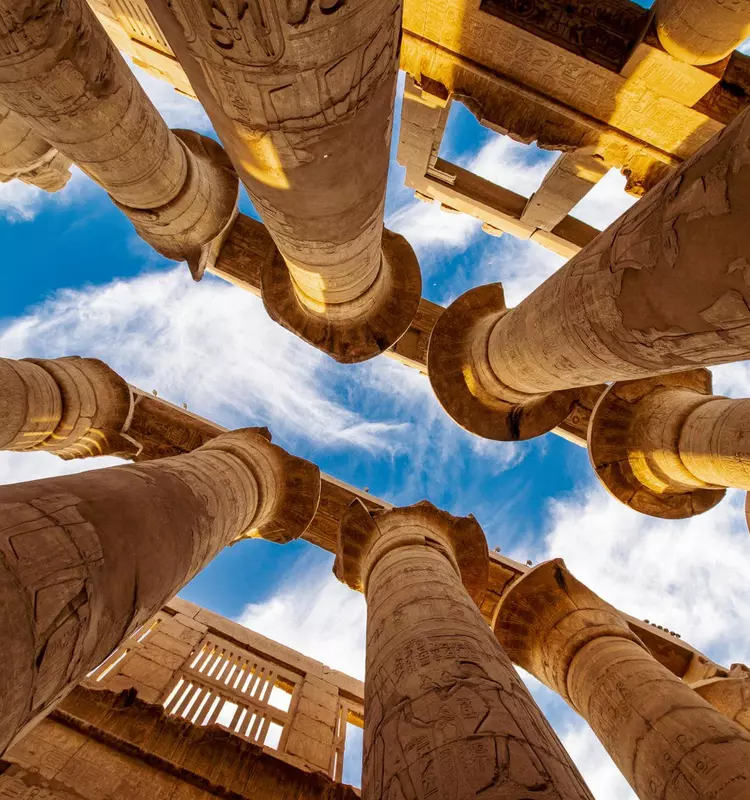 Ancient Egyptian temple columns rise toward a vibrant blue sky, adorned with carved hieroglyphs.