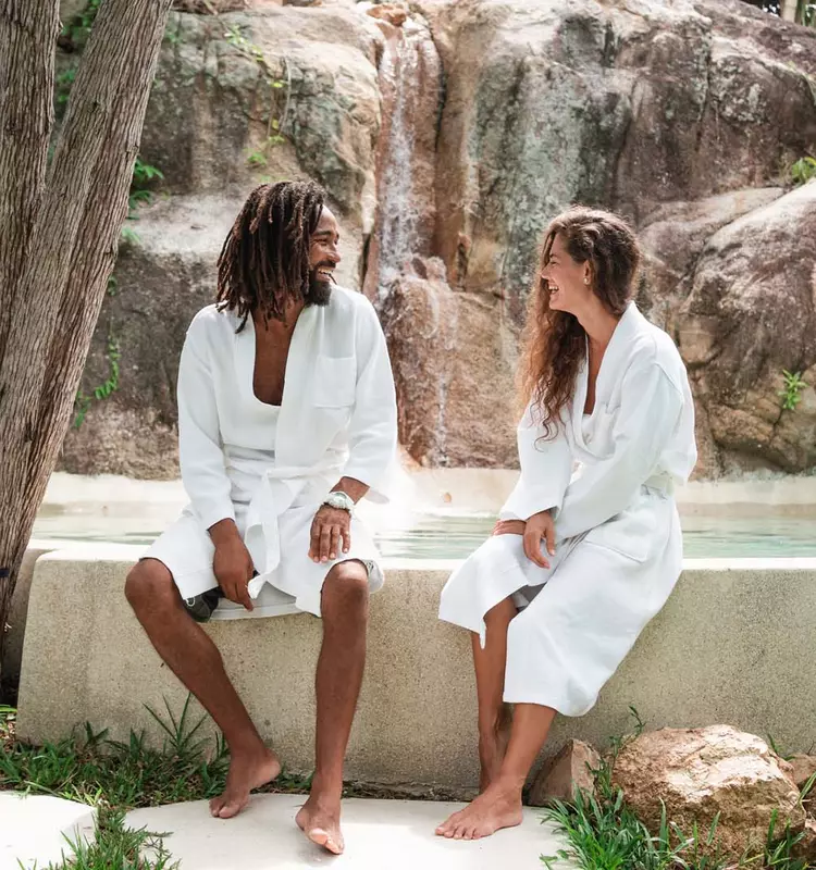 Couple talking, laughing together while relaxing at an outdoor spa, surrounded by nature.