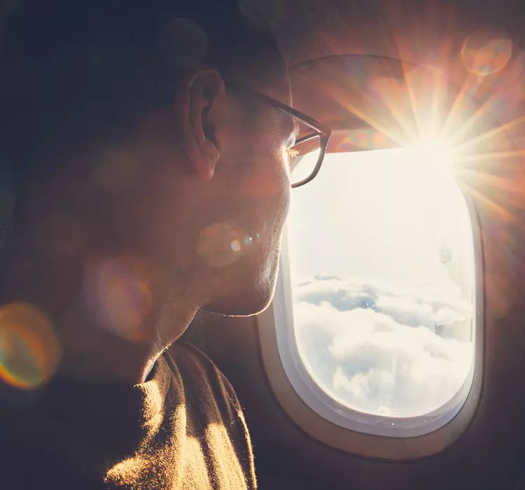 Young man looking out through window of the airplane during beautiful sunrise.