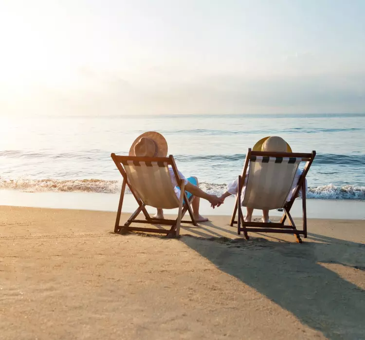 Couple sitting on deck chairs at beach during sunset, watching waves roll in