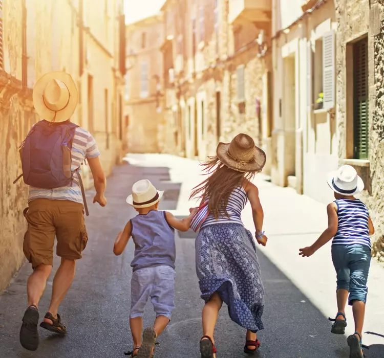 Father and kids running beautiful street of a mediterranean town. Sunny summer day. Pollenca, Mallorca, Spain.