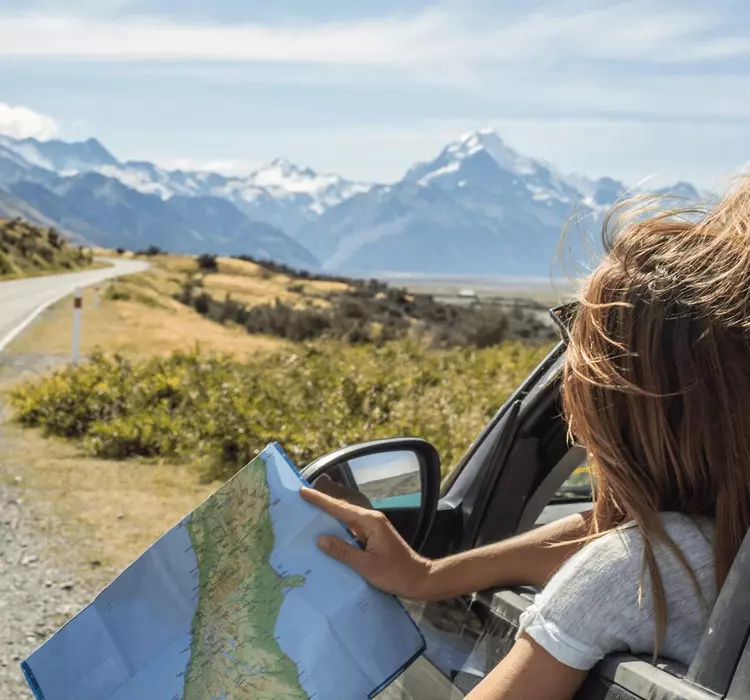 Woman in a car along a highway overlooking a beautiful view, checking a map for directions