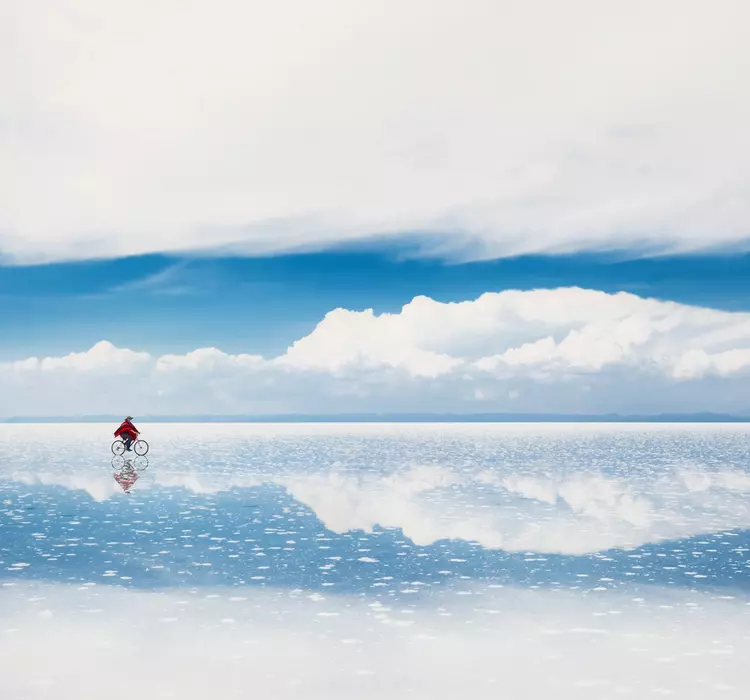 Person walking across salt flats reflecting the sky