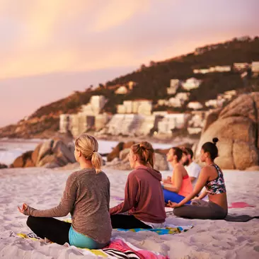 A group of travellers doing yoga on the beach.