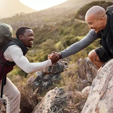 Two men help each other while climbing a mountain