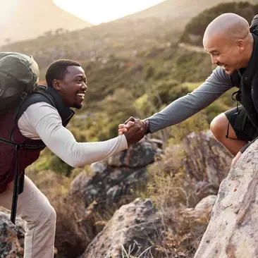 Two men help each other while climbing a mountain