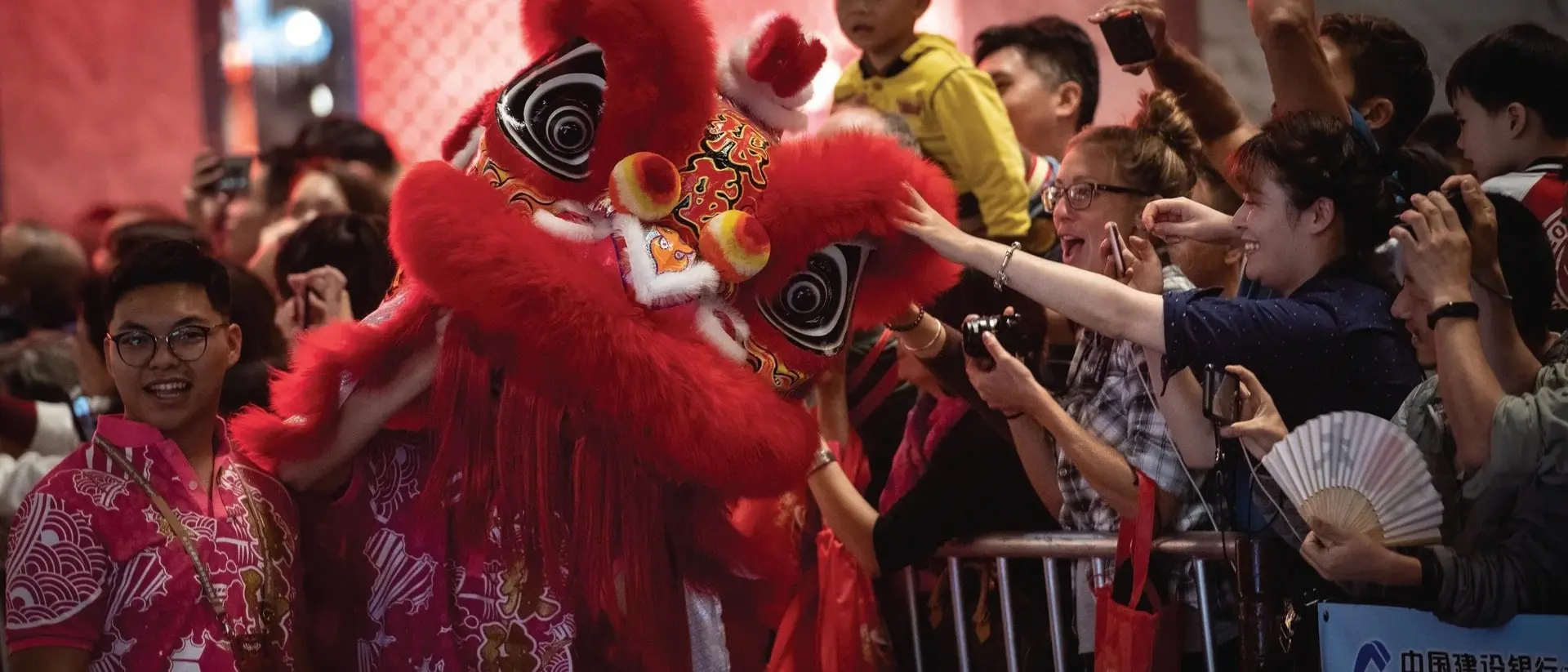 Crowds celebrate at a festival with a vivid red lion dance costume and festive atmosphere.