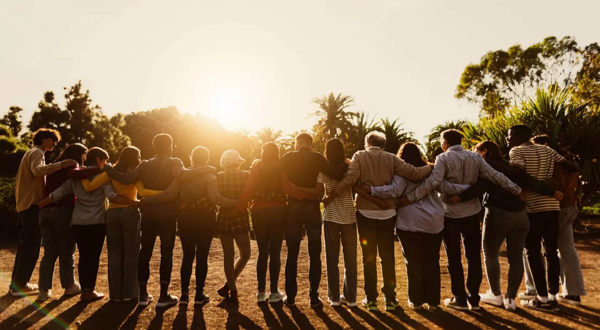 A large group of travellers embrace while watching a sunset