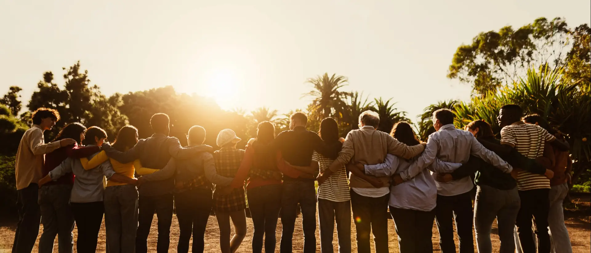 A large group of travellers embrace while watching a sunset