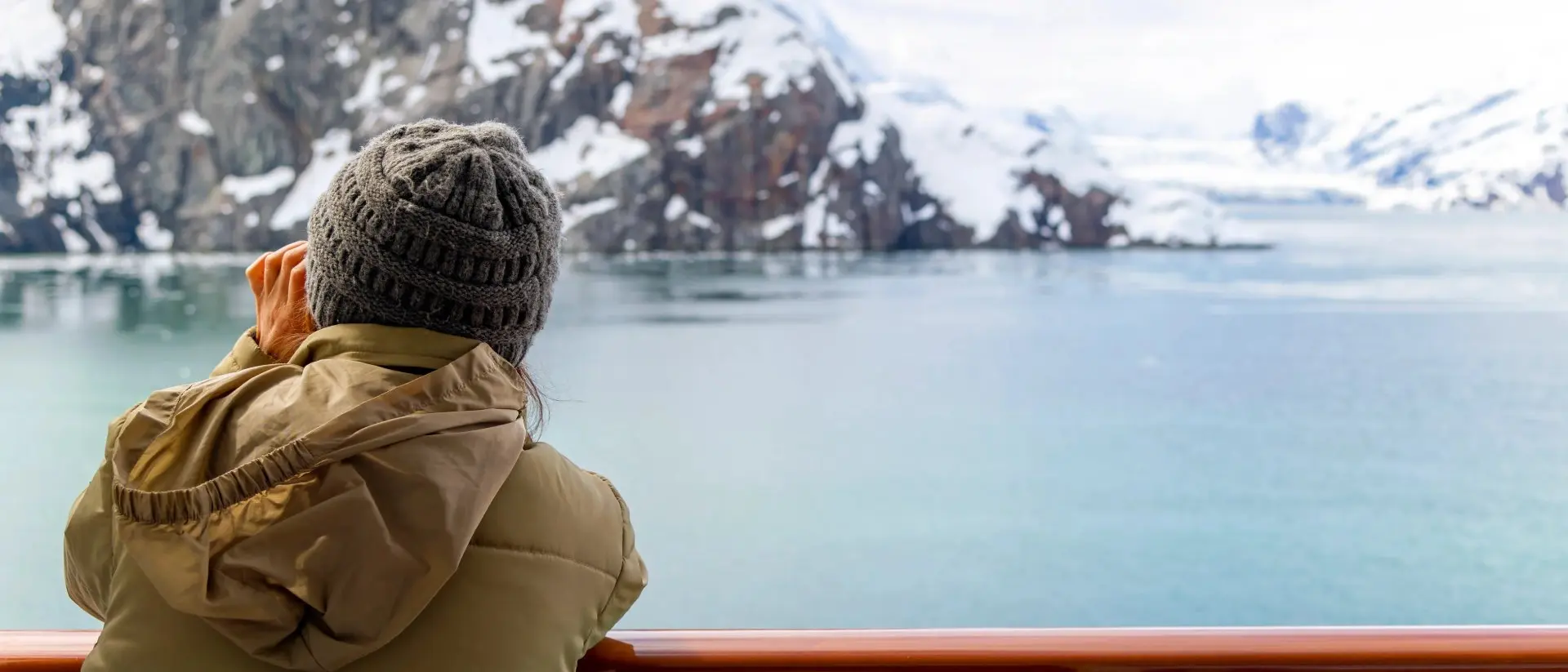 Alaska A young woman with binoculars views the snow covered mountains and glaciers from a cruise ship balcony at Glacier Bay National Park and Reserve, Alaska USA.