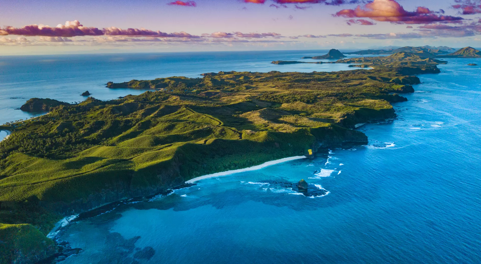 Aerial view of a Fiji island with bright green foliage and sunset sky