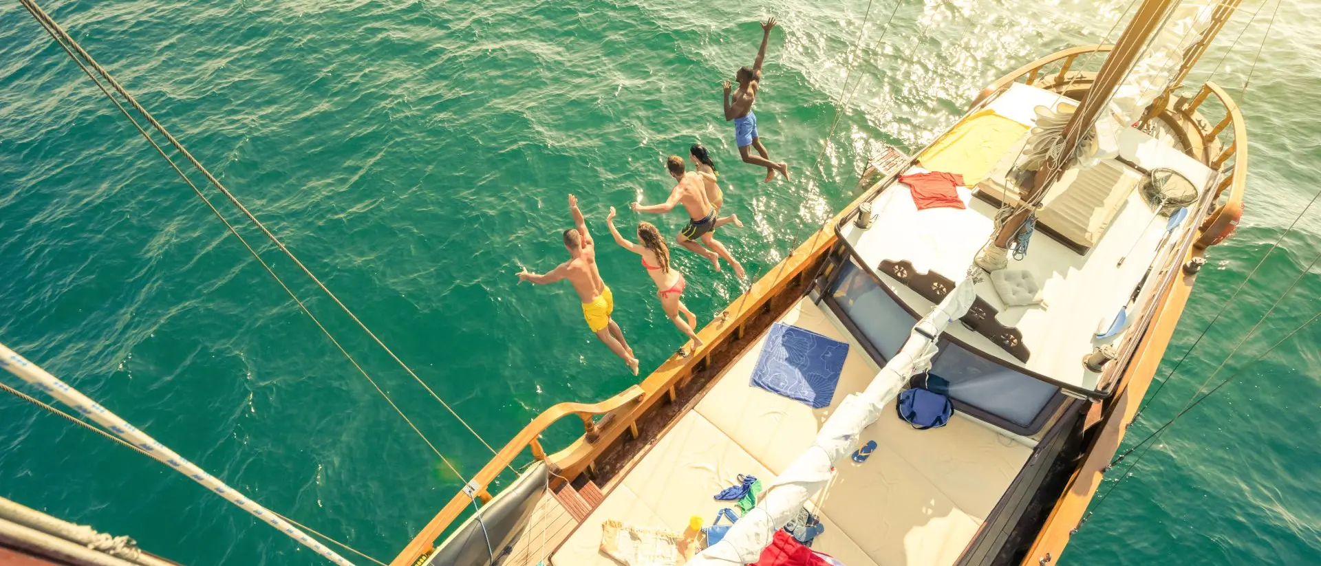 Aerial view of group of people jumping from sailing boat on a day sea trip