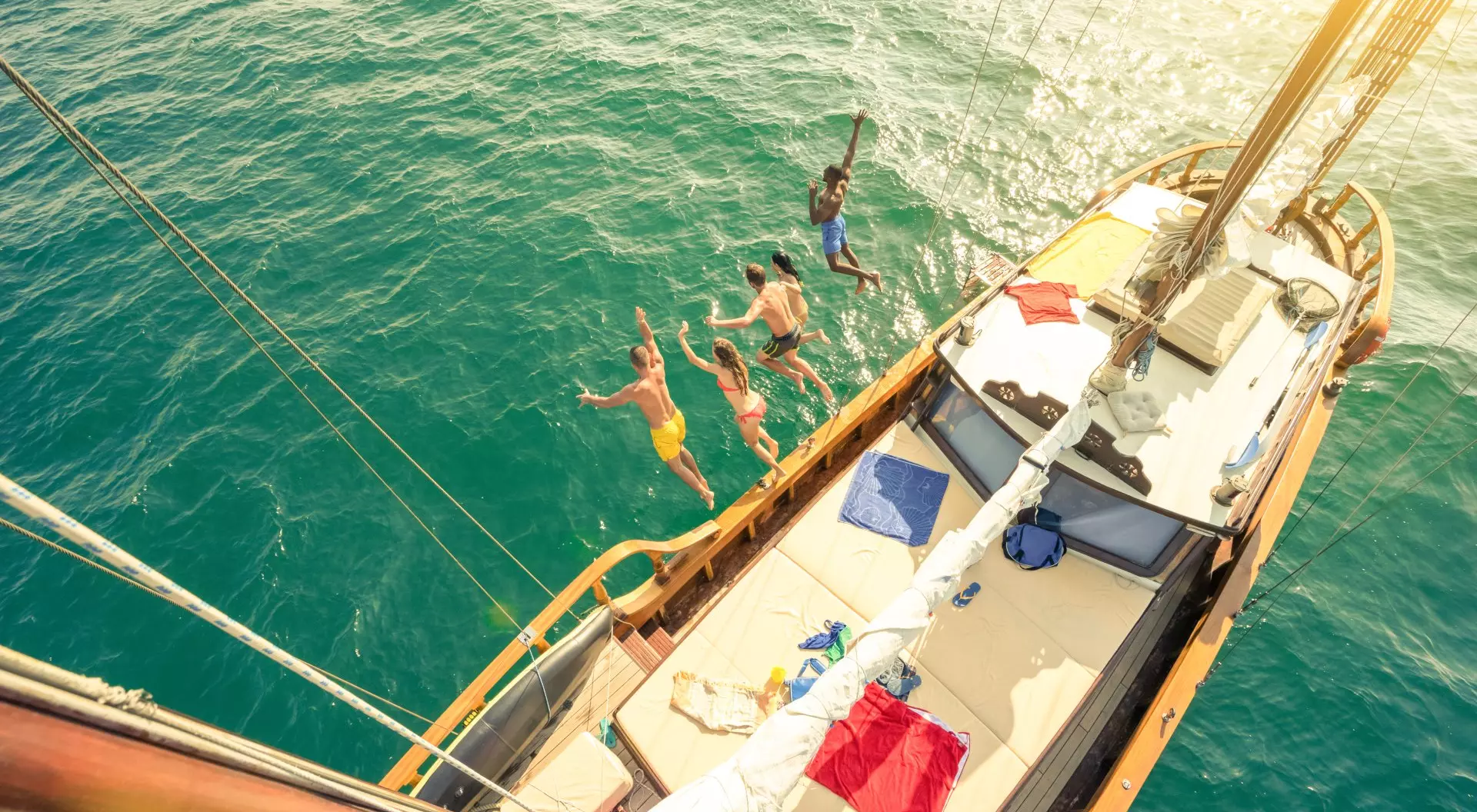 Aerial view of group of people jumping from sailing boat on a day sea trip