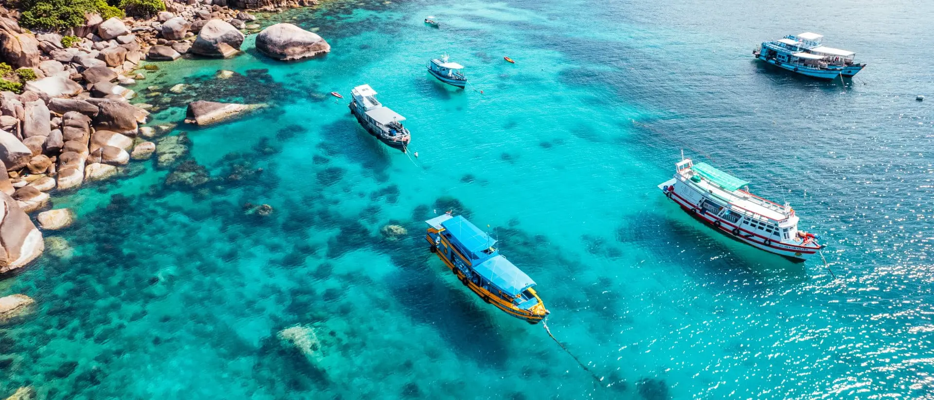 Boats and crystal clear waters at the bay dive site from above