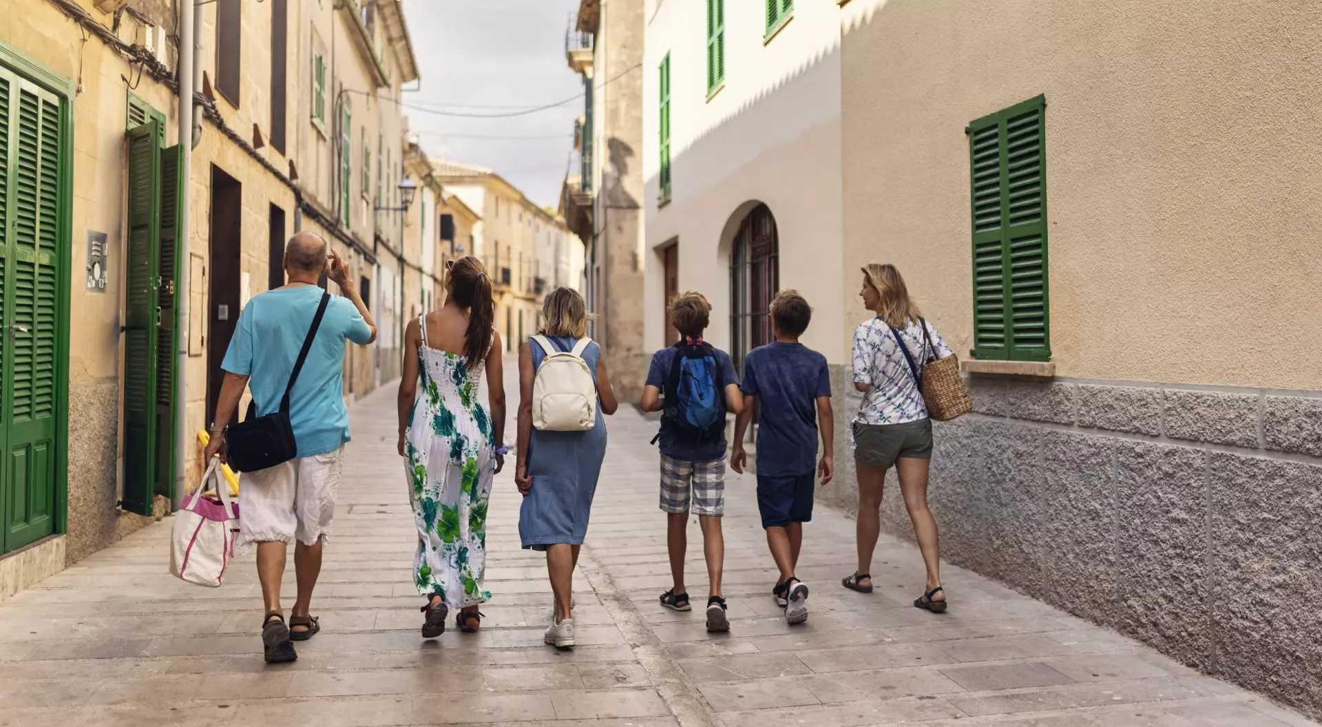 Family walking in beautiful town of Alcudia. Sunny summer day in Majorca, Spain. Mother, grandparents and three teenagers are walking in narrow street