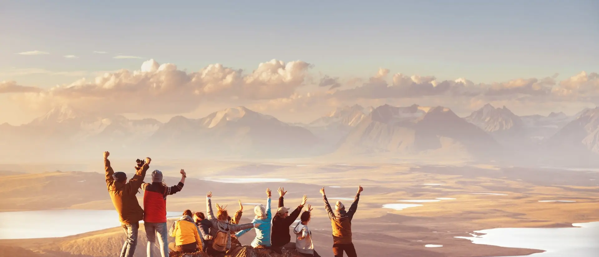 Group celebrating hiking to reach top of mountain top looking out at mountain's valley