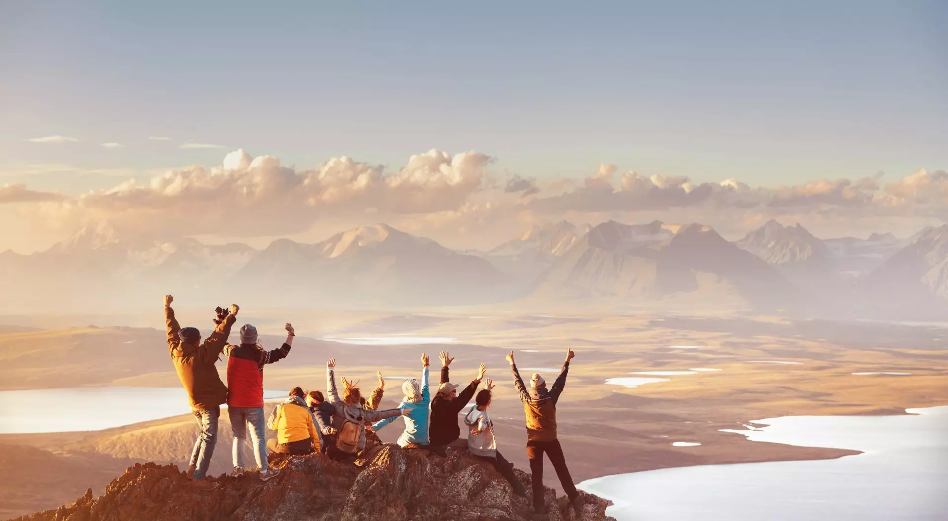 Group celebrating hiking to reach top of mountain top looking out at mountain's valley