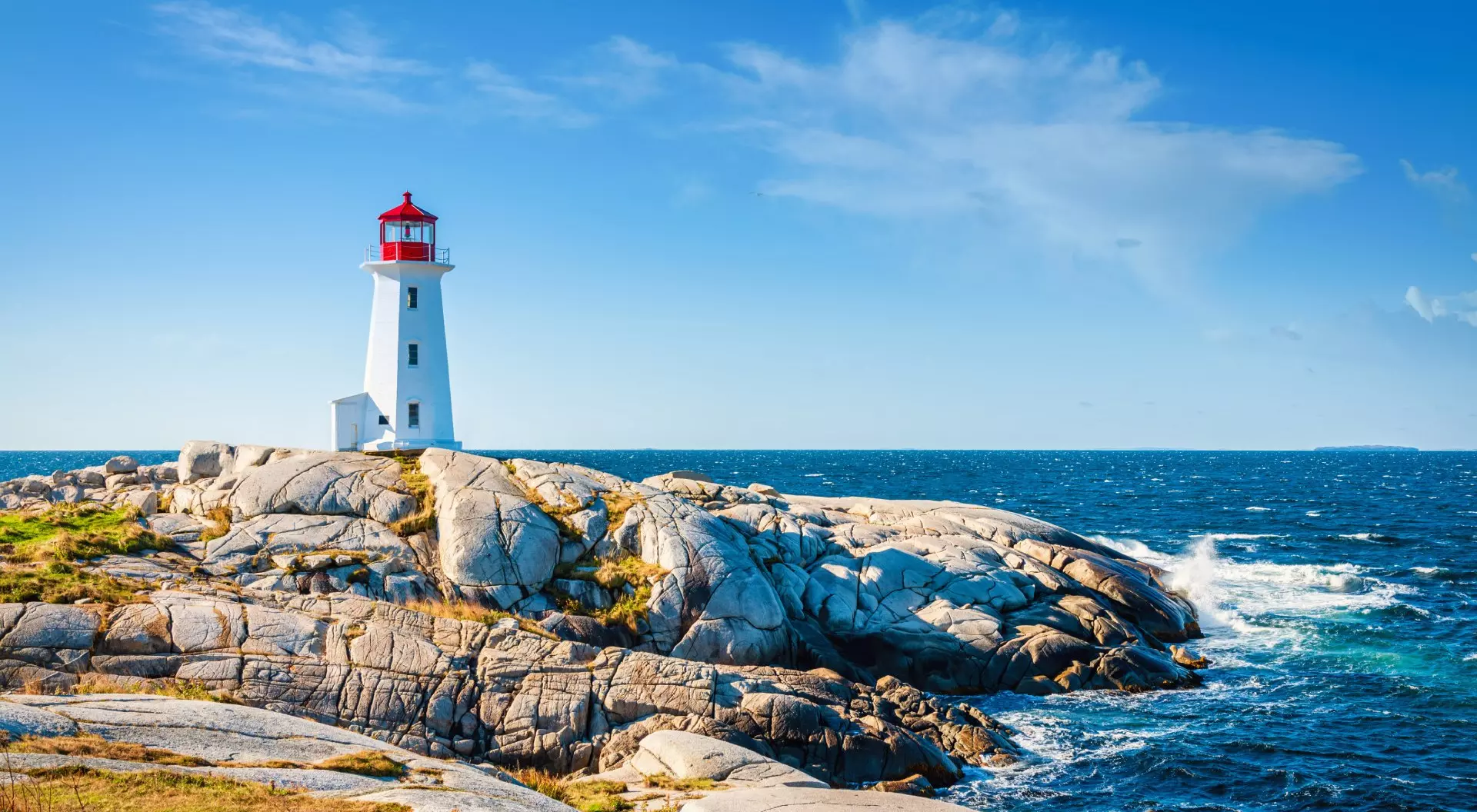 Peggy's Cove Lighthouse under blue summer sky on the coast of the Atlantic Ocean.