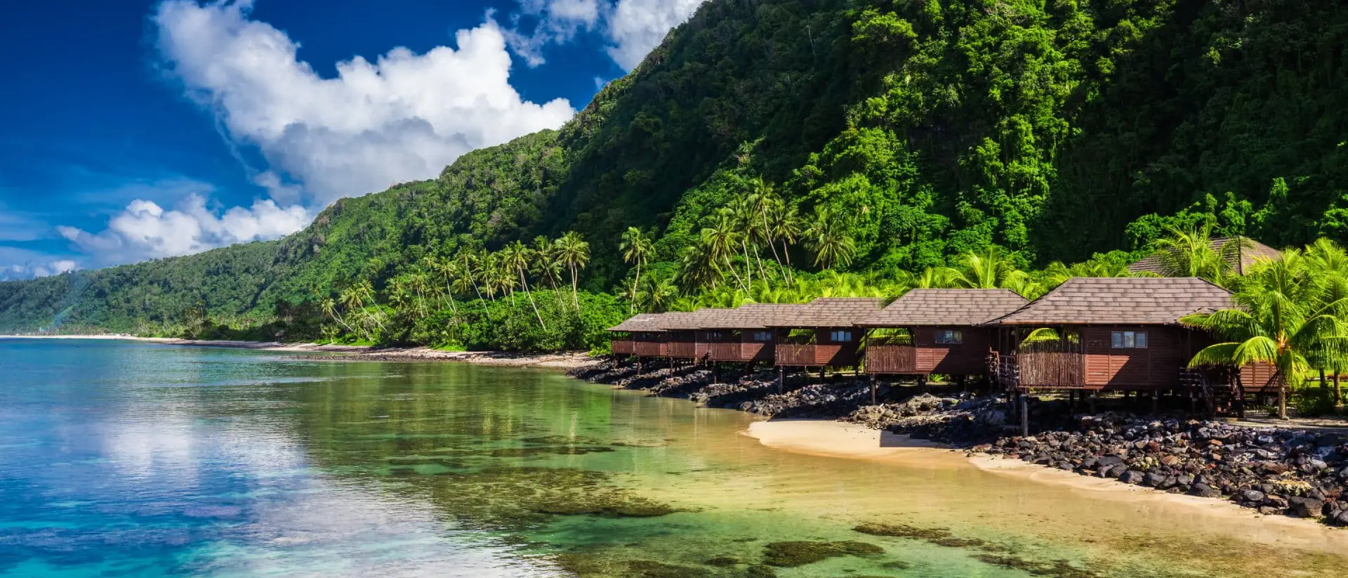 Lalomanu Beach Small beach houses line the shore with green vegetation behind them