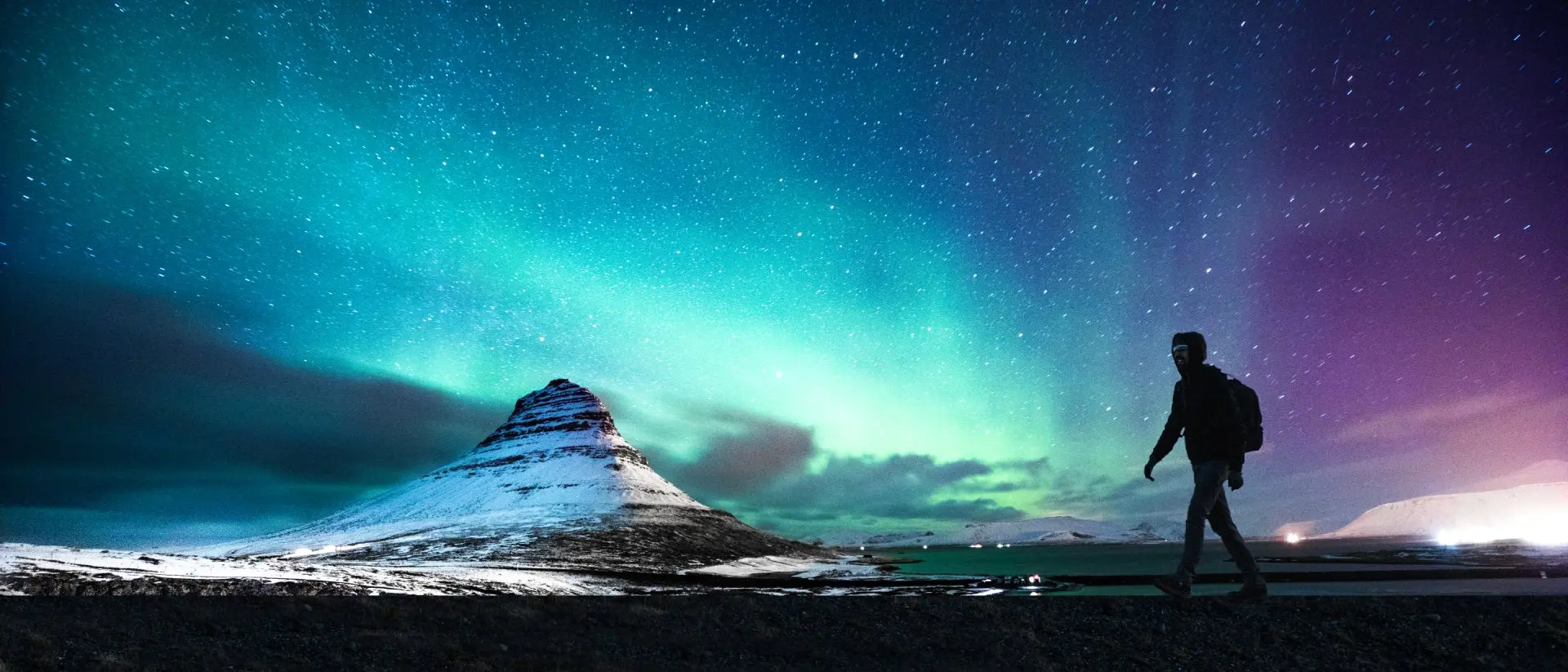 Solo traveler walking in front of an awesome Northern Lights in Mount Kirkjufell Iceland.