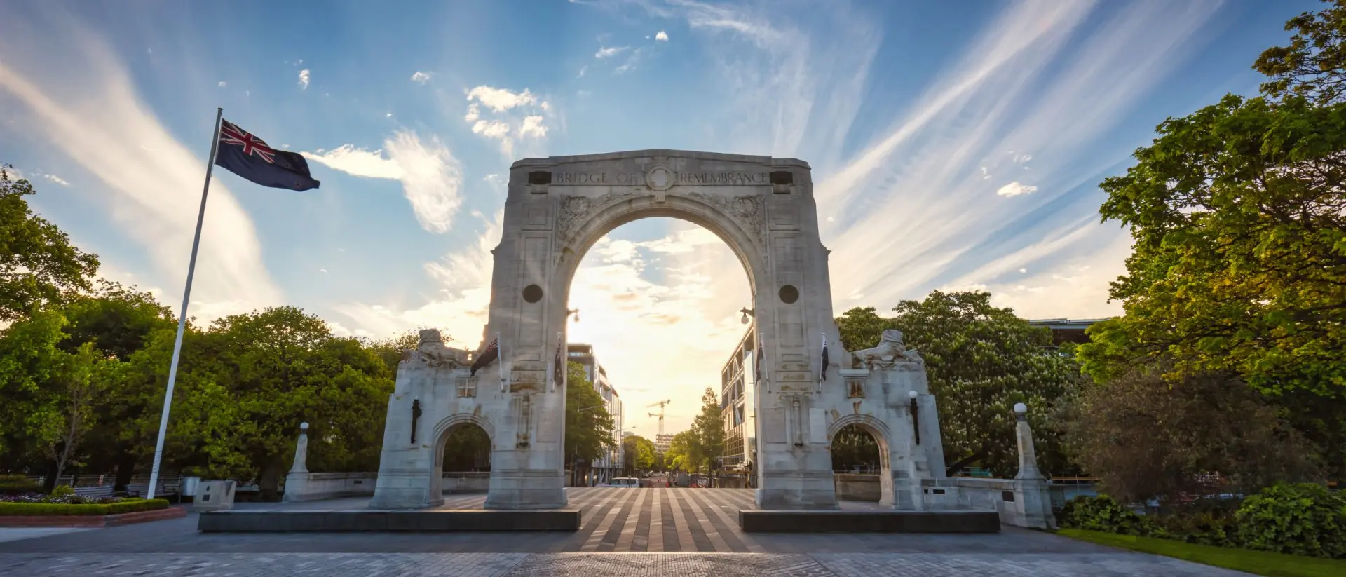 Sunset Panorama of the famous Bridge of Remembrance in Christchurch with New Zealand Flag blowing in the wind. Arch backlit against the sunset Sun
