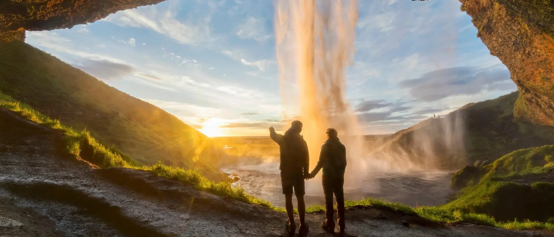 Tourists under waterfall in Seljalandsfoss, Iceland, man pointing with finger to the sun