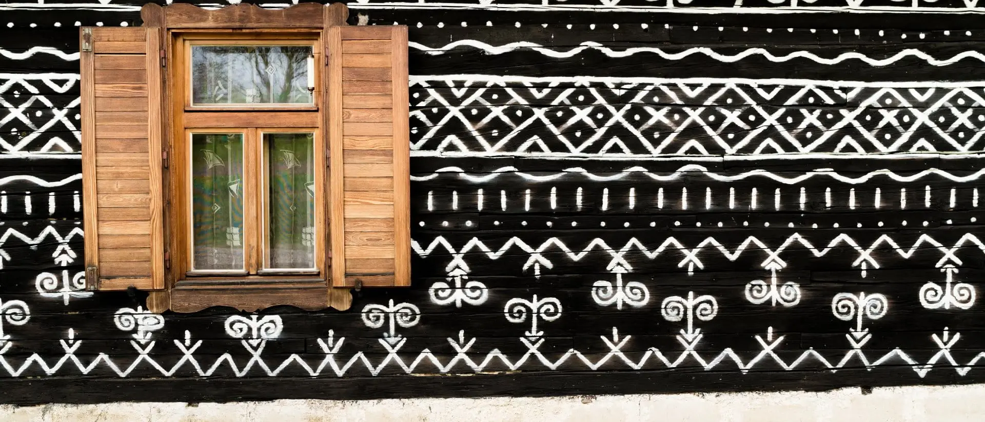 Cicmany, Slovakia Wooden window on the White and black pattern ornament painting on the dark wood wall in Slovakian old village Cicmany