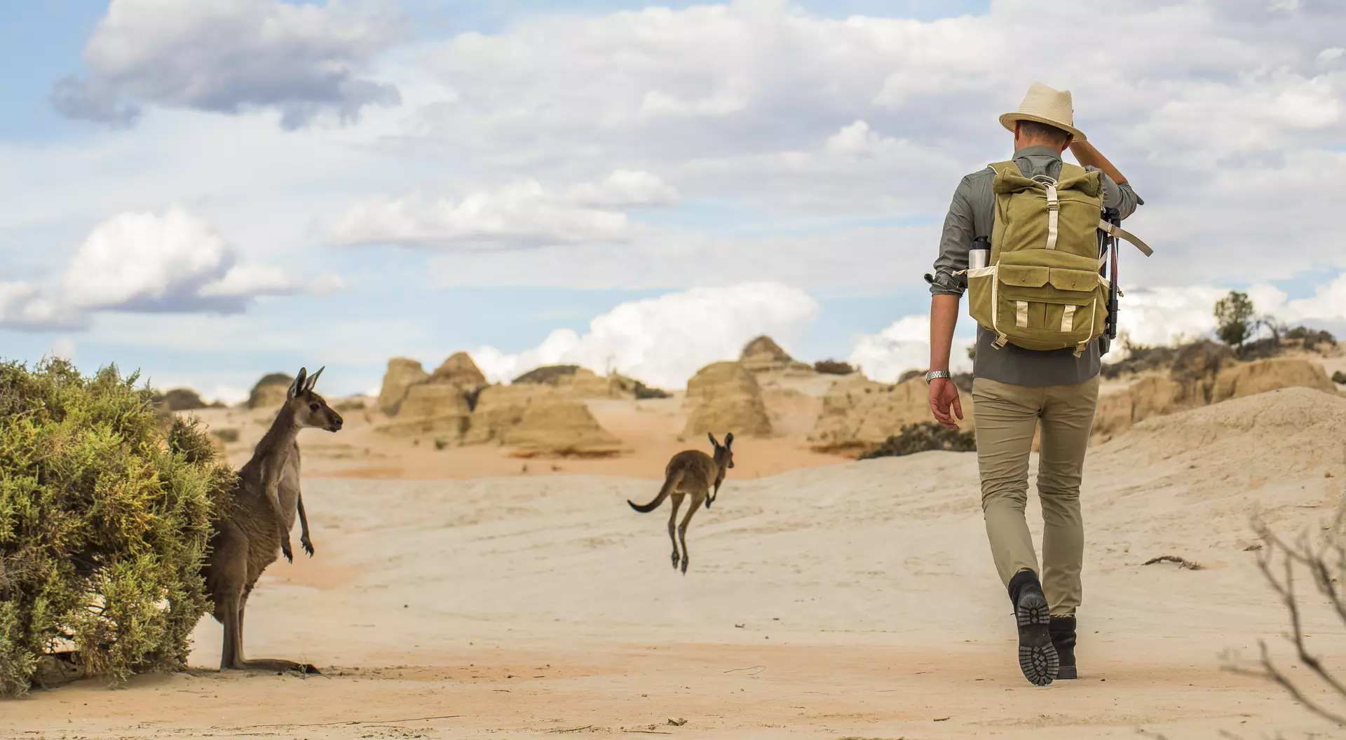 Young man walking in arid desert landscape with photography backpack on an adventure in outback Australia