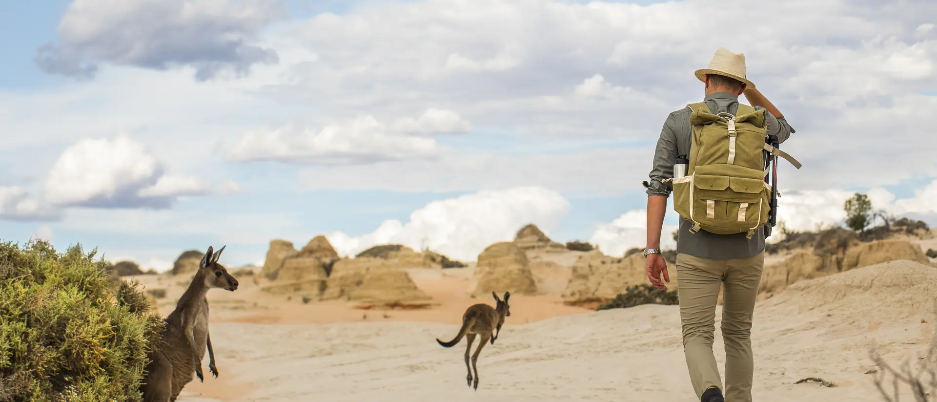 Young man walking in arid desert landscape with photography backpack on an adventure in outback Australia