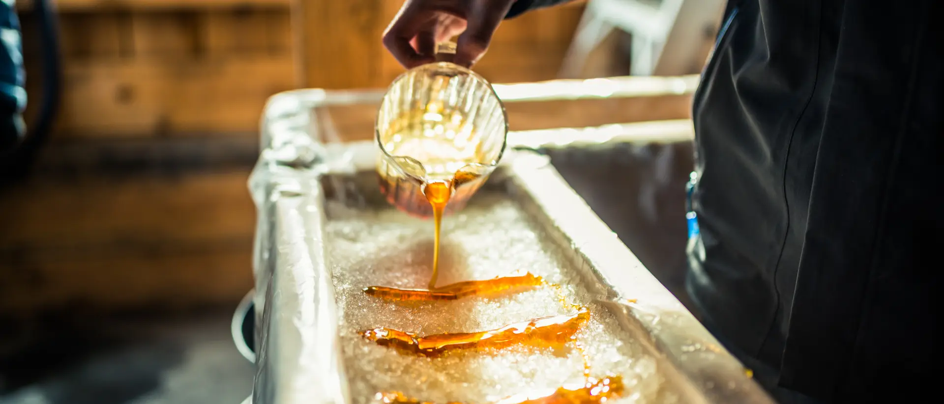Person pouring maple syrup onto snow at sugar shack
