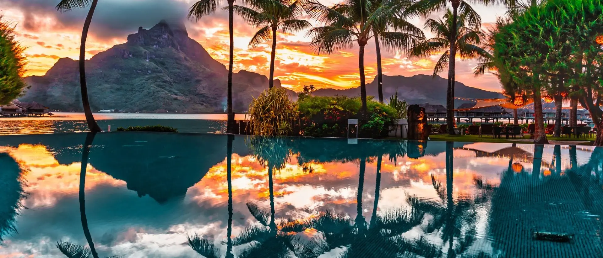 Beautiful sunrise over a pool with palm trees and mountains in the background.