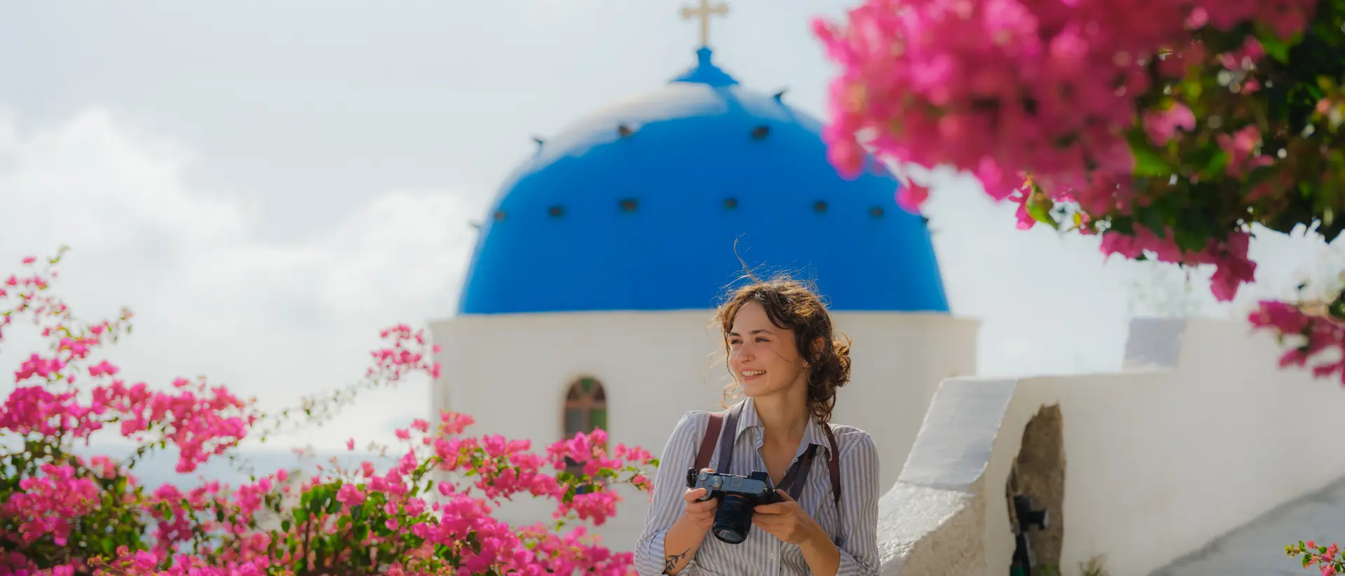 Oia, Santorini A woman leaning on the edge of a walkway in Oia on Santorini in Greece with bouganvillea blooming