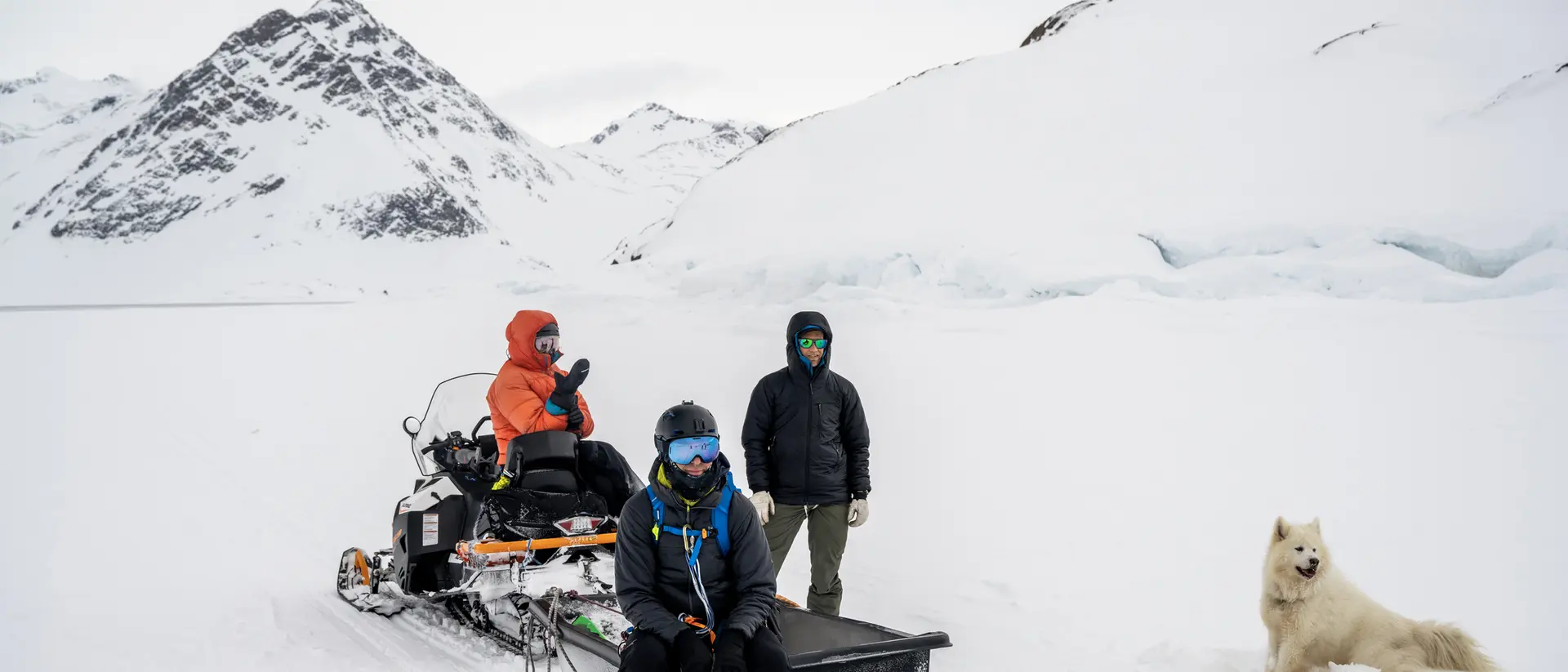 A group of people wait for their dogs to return after dogsledding across the winter landscape in Greenland.