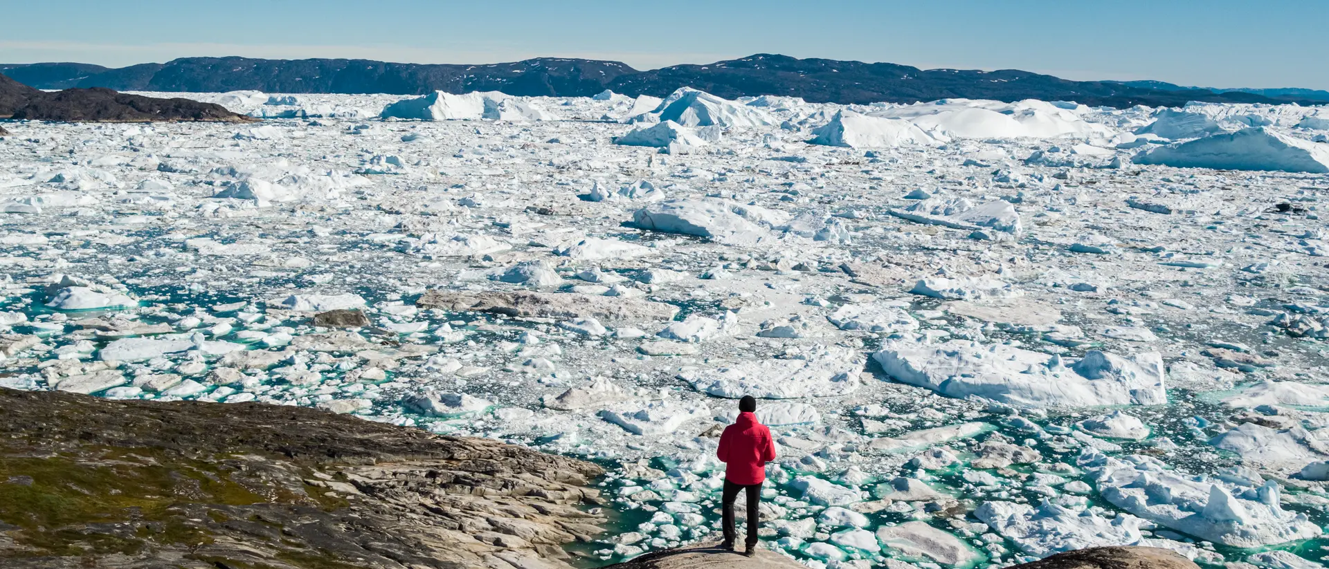 Ilulissat is known for its iceberg flows, which calve off the nearby glaciers. A man stands on the edge of the water watching icebergs in the waters off the town of Ilulissat in central Greenland.