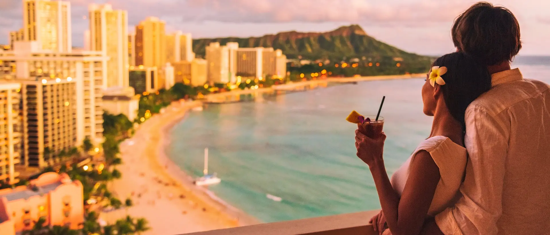 Waikiki, Hawaii Embraced couple enjoying a sea-side view from a balcony, overlooking a city skyline and sunny sky.