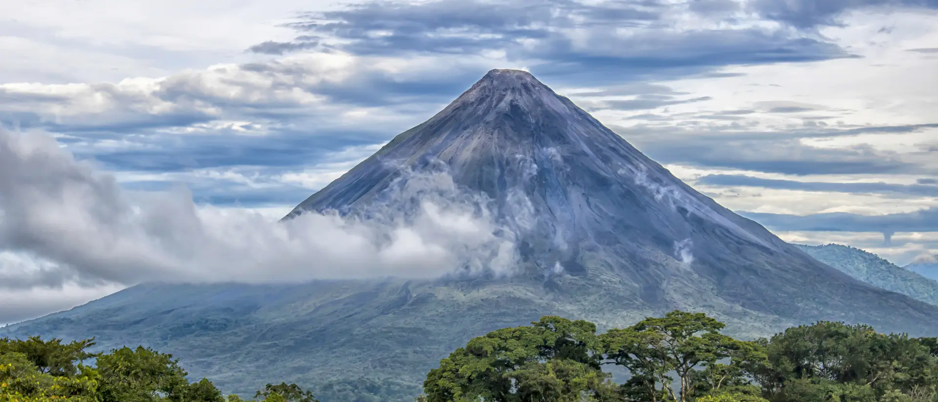 Rainforest, volcano rising in distance with clouds surrounding