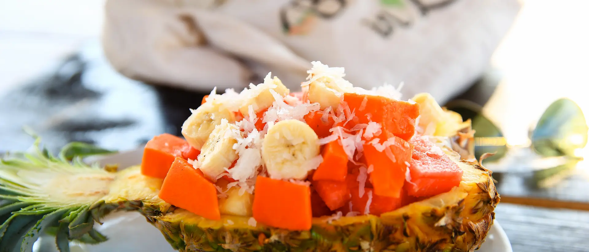 A halved pineapple filled with banana, papaya, and coconut shavings, with a lime slice on a plate.