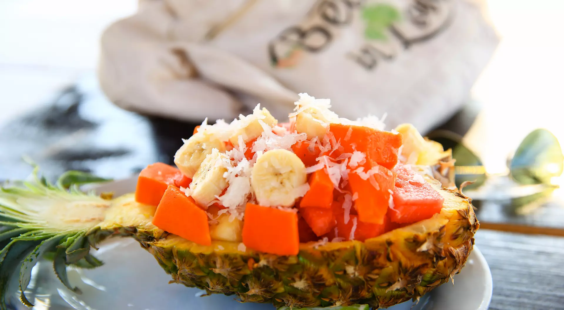 A halved pineapple filled with banana, papaya, and coconut shavings, with a lime slice on a plate.
