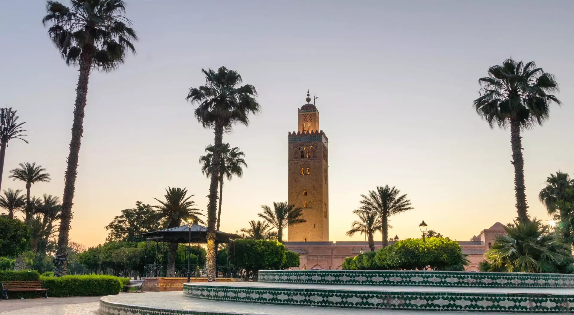 A view of a tall tower surrounded by palm trees and greenery at sunset.