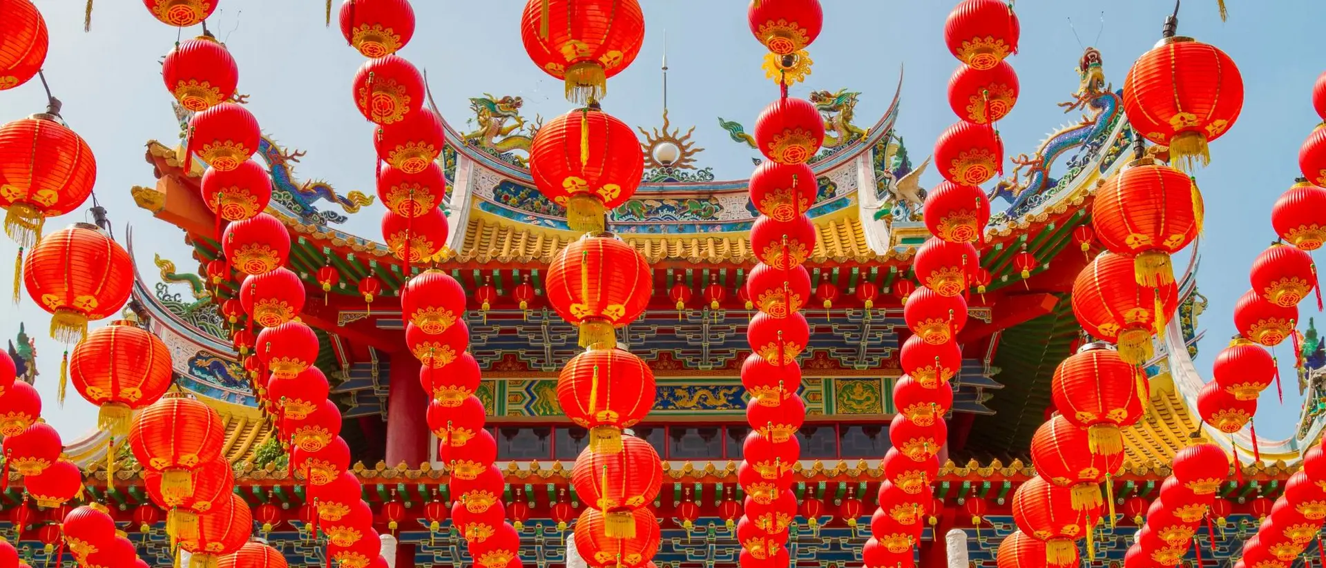 A vibrant display of red lanterns hanging in front of a decorative building, celebrating a festive occasion.