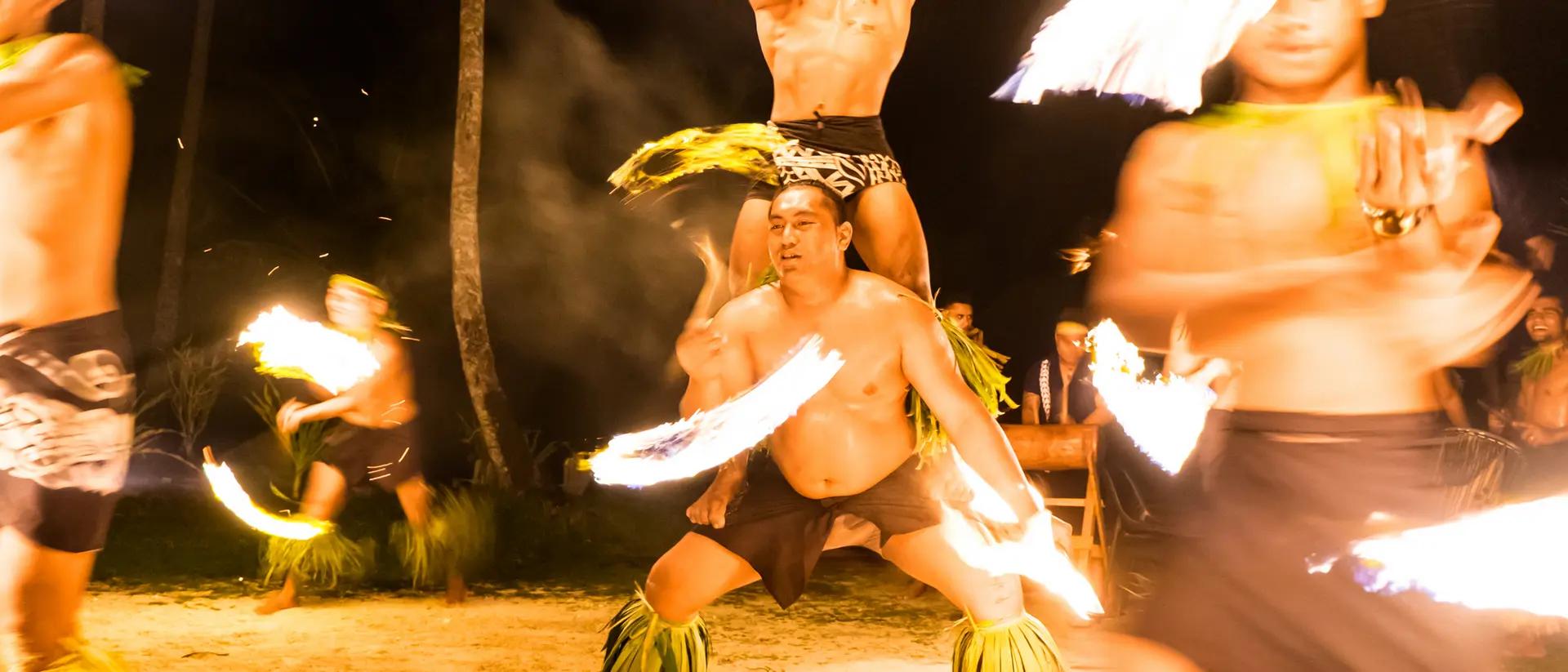 Fire dancers perform rhythmic movements under the night sky, creating glowing trails with flaming torches.
