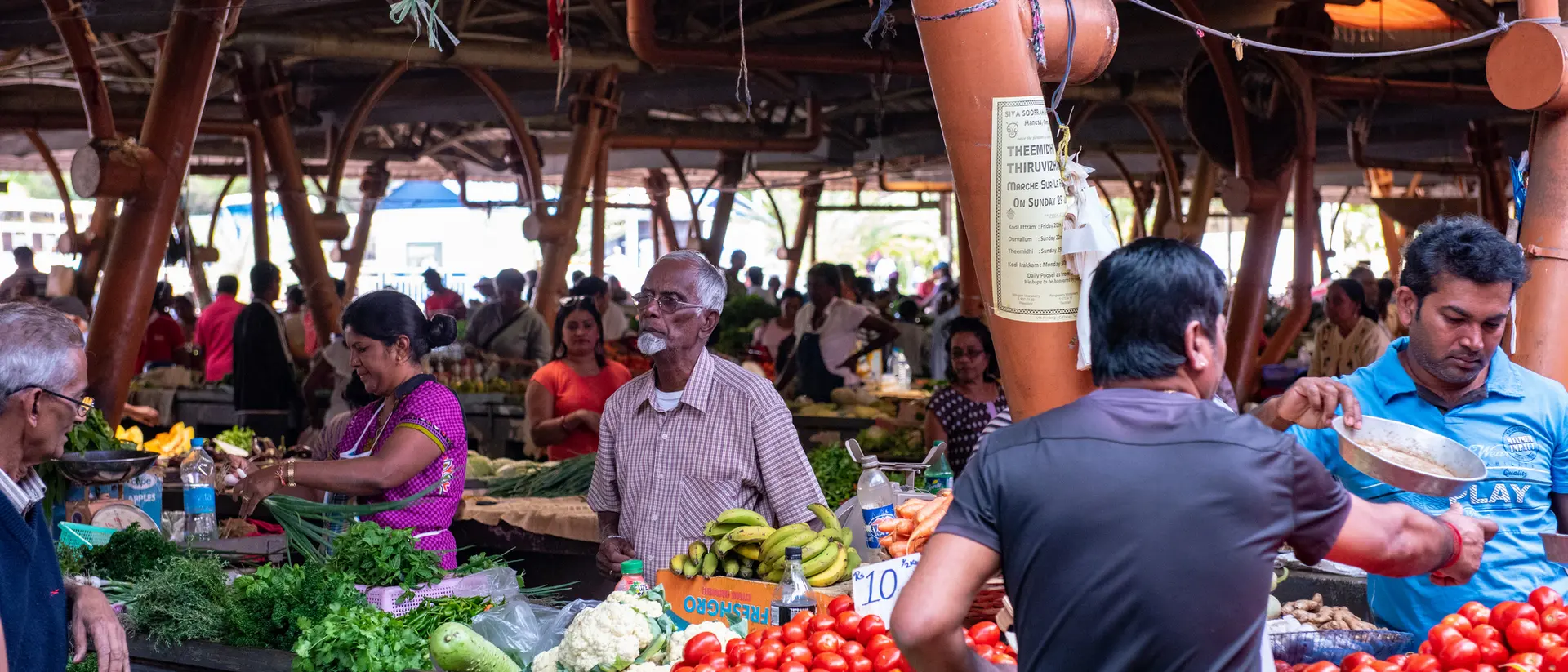A vibrant market scene with people shopping for fresh vegetables and fruits at various stalls.
