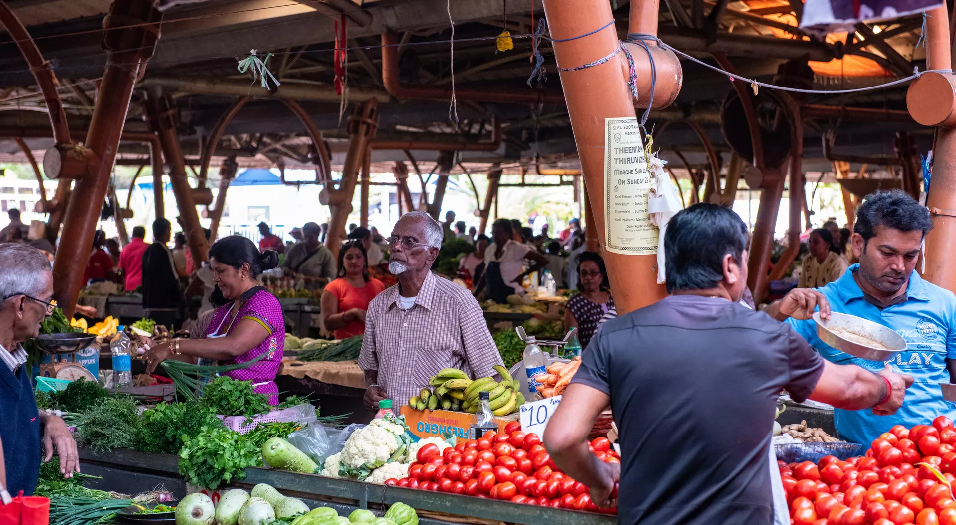 A vibrant market scene with people shopping for fresh vegetables and fruits at various stalls.