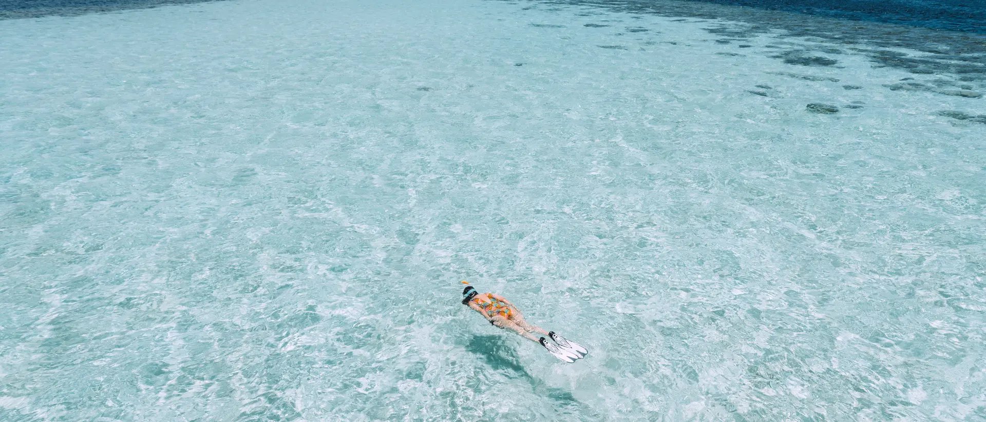 Person snorkeling in clear turquoise waters, surrounded by a vibrant ocean under a blue sky.