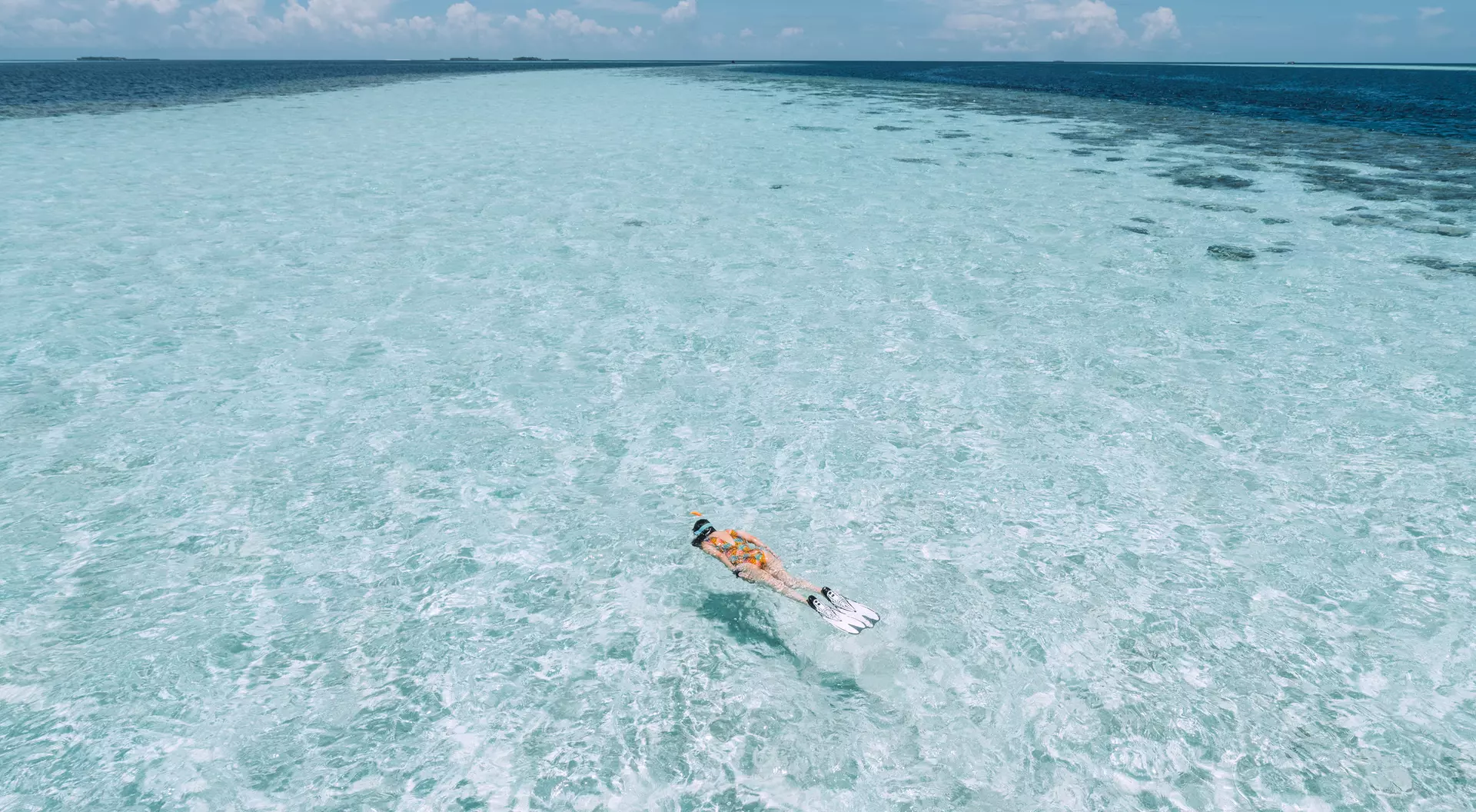 Person snorkeling in clear turquoise waters, surrounded by a vibrant ocean under a blue sky.