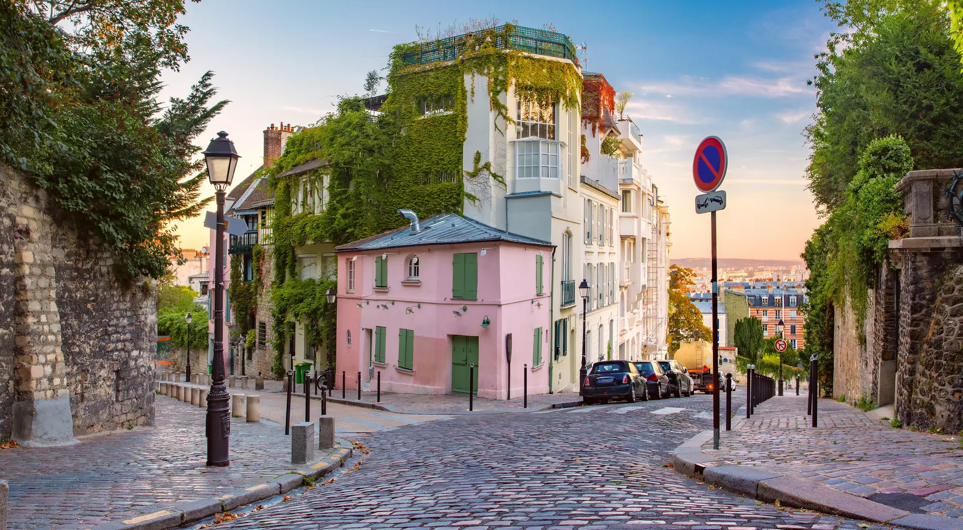 A charming cobblestone street in a picturesque neighborhood with lush greenery and pastel-colored buildings.